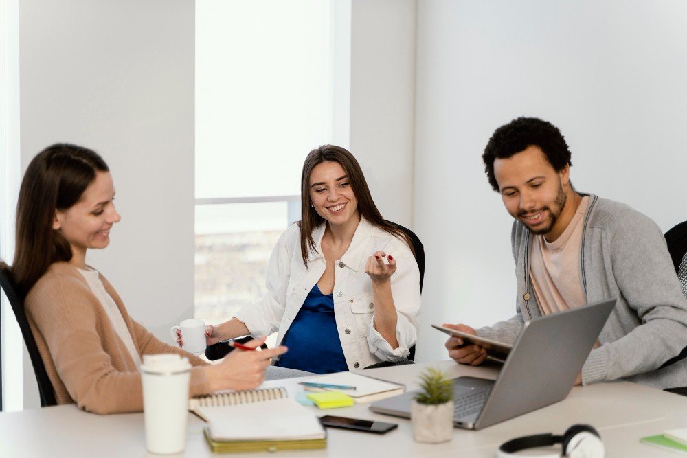 smiling-colleagues-discussing-work-while-using-laptop-and-tablet-in-office