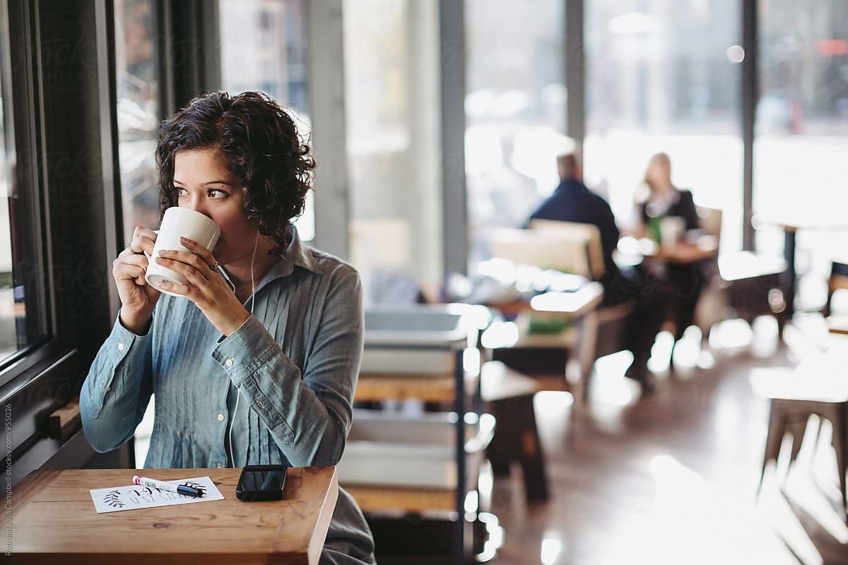 woman-with-curly-hair-sipping-mug-by-window-looking-outside