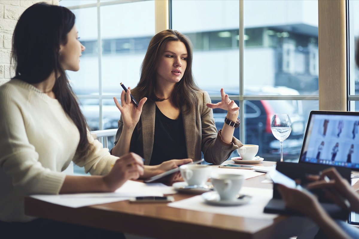 two-professional-women-having-a-discussion-in-modern-office-near-window