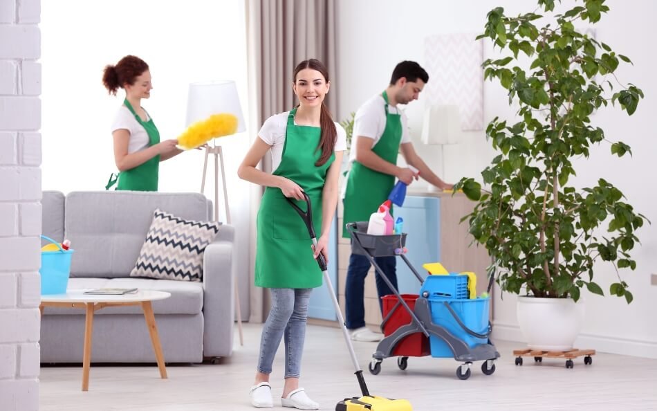 Smiling female cleaner mopping a floor while a male cleaner works in the background.
