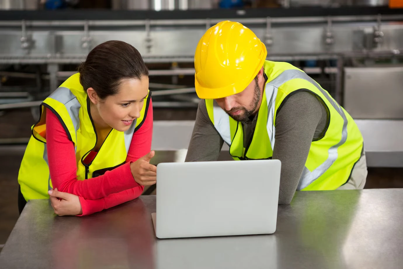 man-and-woman-in-safety-vests-and-hard-hat-reviewing-laptop-in-industrial-setting