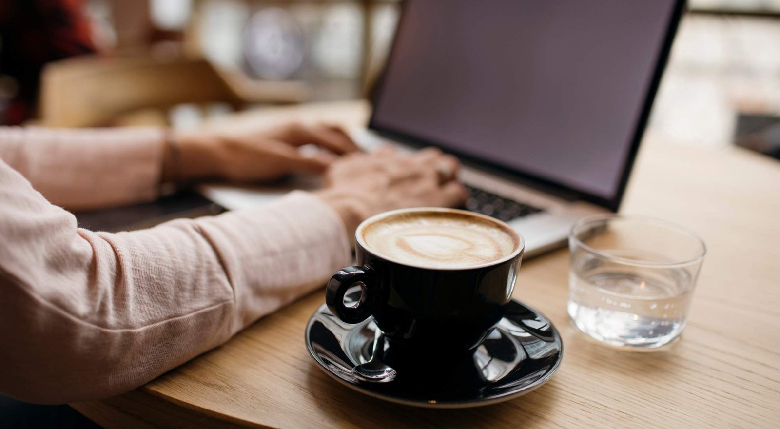 black-coffee-mug-in-focus-hands-typing-on-laptop-in-background