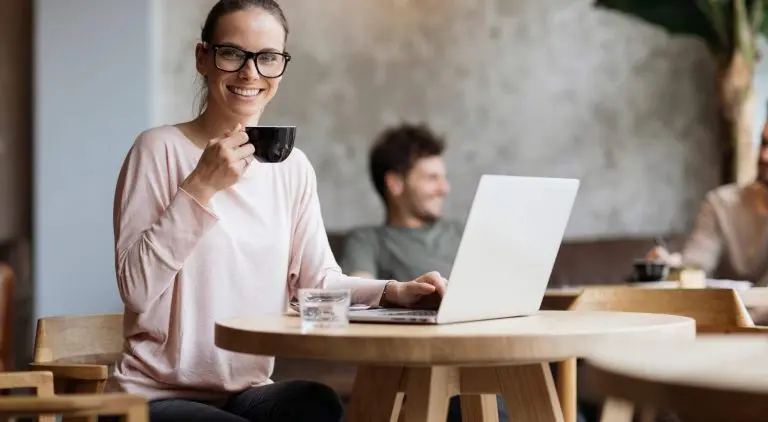 woman-smiling-holding-black-mug-working-on-laptop-in-café
