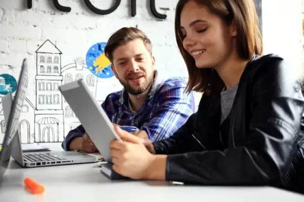 Two young digital marketers in Regina collaborating using a tablet and laptop in a modern creative workspace