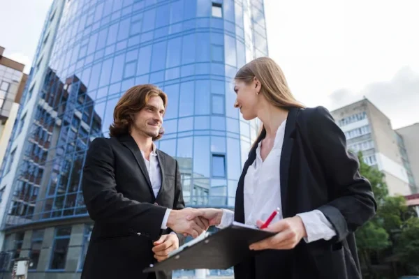 Two business professionals in Regina shaking hands in front of a modern glass office building