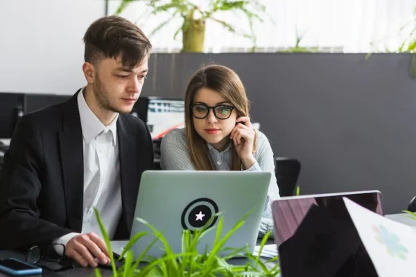Two professionals working on a laptop in a modern Regina office, discussing project details and planning SEO strategies for local businesses.