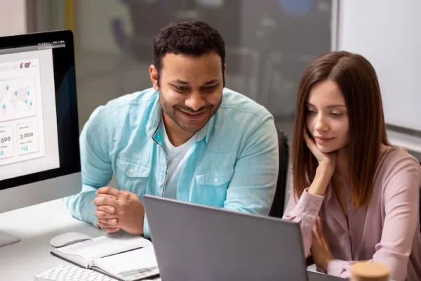 Two professionals reviewing data on a laptop in a Regina office while conducting keyword research and market evaluation for a local business.
