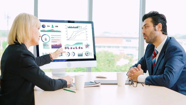 Two SEO experts reviewing digital campaign performance charts on a large computer screen during a strategic meeting.