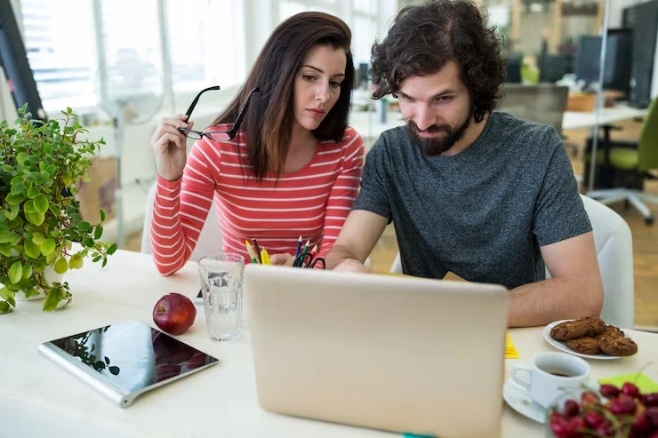 Two SEO experts reviewing ideas on a laptop in a creative workspace while discussing content development strategies.