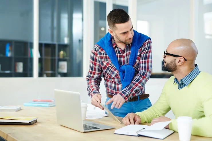 Marketing specialists discussing website content strategy for metal fabrication services using a laptop and documents.