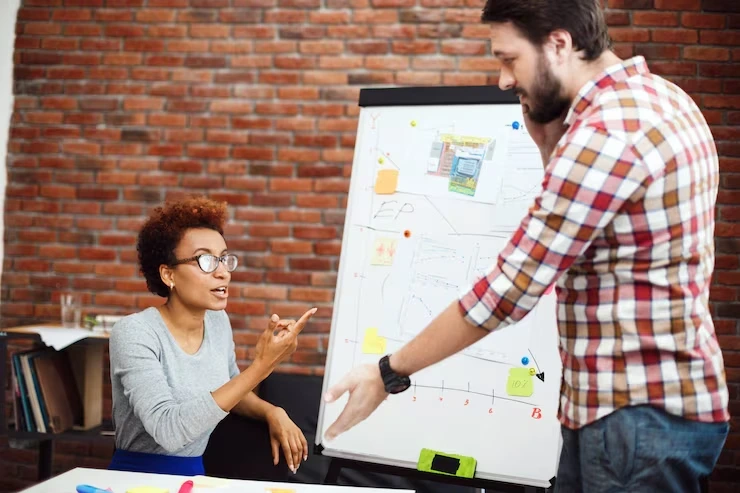 Two professionals discussing website improvements on a laptop, symbolizing businesses planning effective Schema Markup Strategy Development.