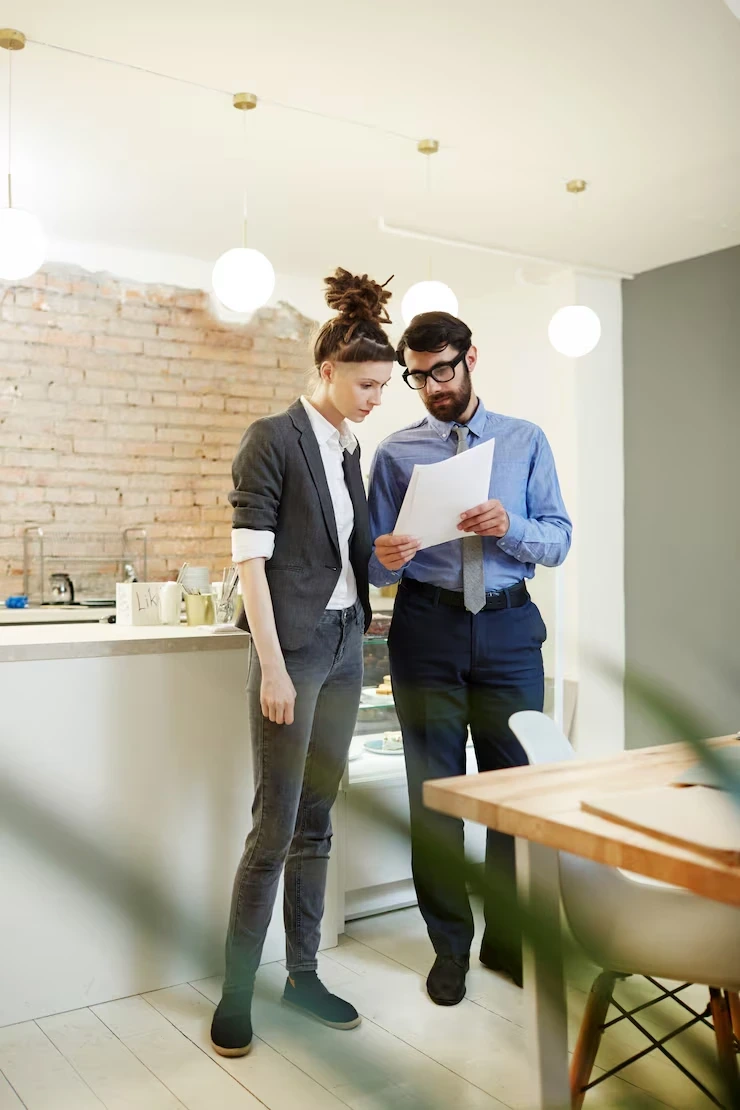Two professionals standing together and reviewing documents in a modern office environment, discussing business strategy.